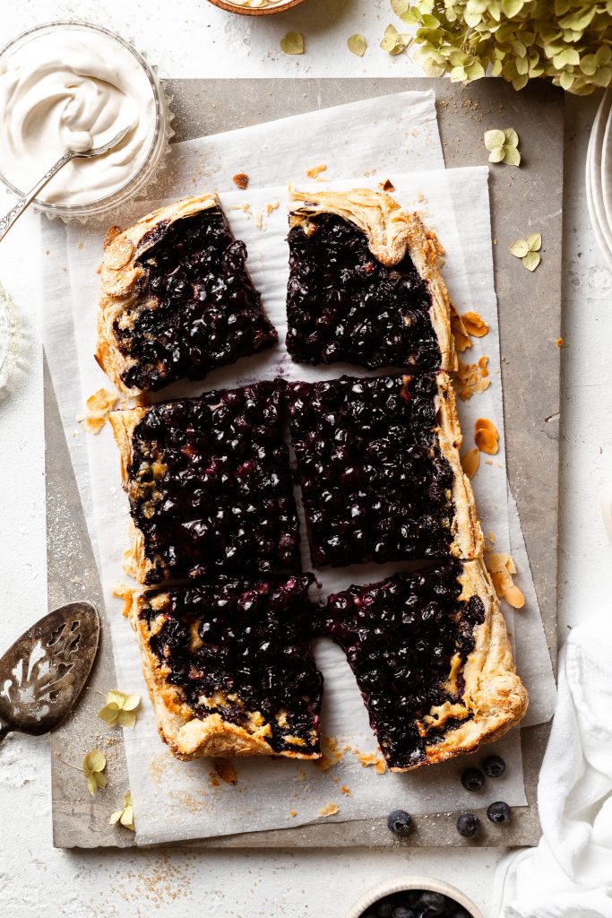 Sliced open face pie on a piece of parchment paper, beside a silver serving spatula. 