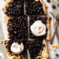 Berry tart into 6 large pieces, 2 of which are dolloped with whipped cream.
