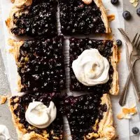 Berry tart into 6 large pieces, 2 of which are dolloped with whipped cream.