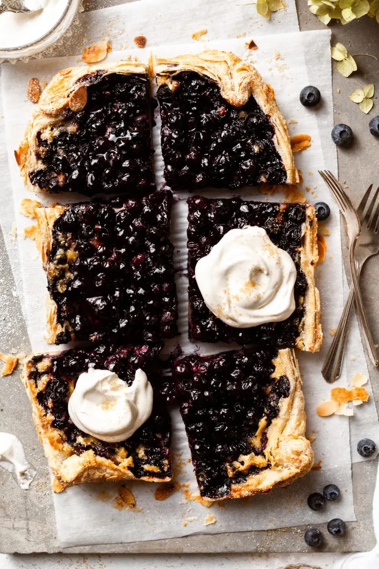 Berry tart into 6 large pieces, 2 of which are dolloped with whipped cream.