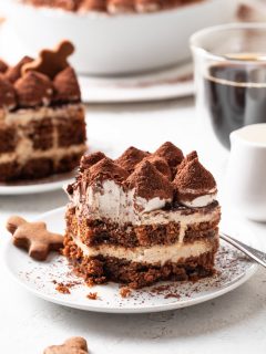A serving of tiramisu missing a bite on a white plate beside a gingerbread cookie.