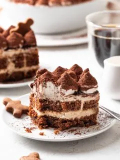 A serving of tiramisu missing a bite on a white plate beside a gingerbread cookie.