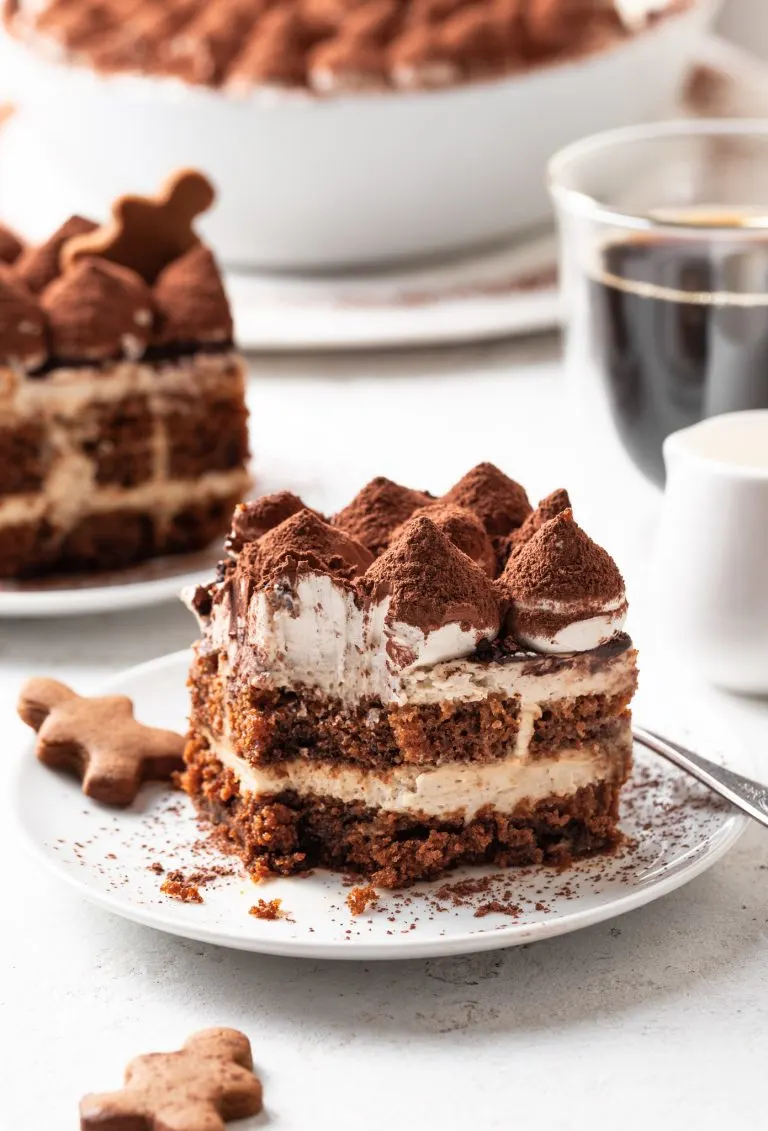 A serving of tiramisu missing a bite on a white plate beside a gingerbread cookie.
