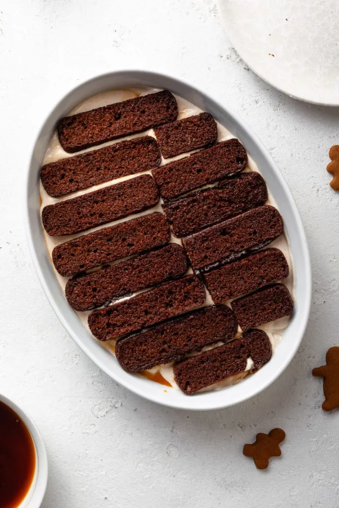 A layer of gingerbread cookies on top of a creamy filling in a white baking dish.