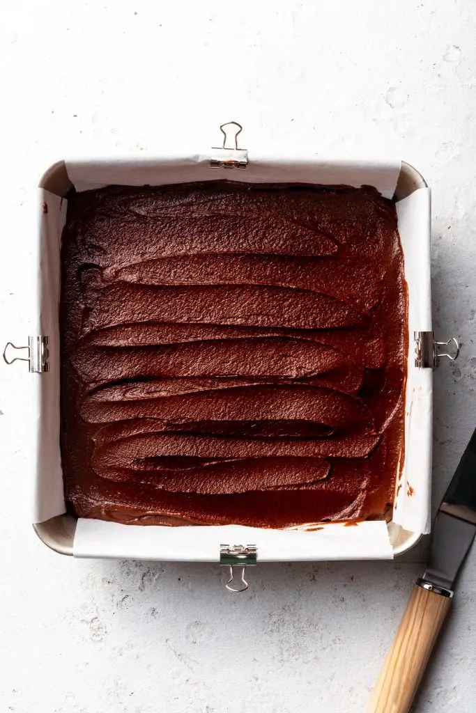 A square baking tin filled with raw brownie batter. 