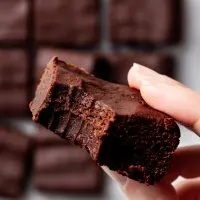 View of someone holding a brownie with a bite missing, over a batch of brownies.