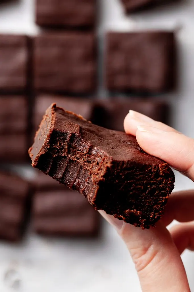 View of someone holding a sweet potato brownie with a bite missing, over a batch of brownies.