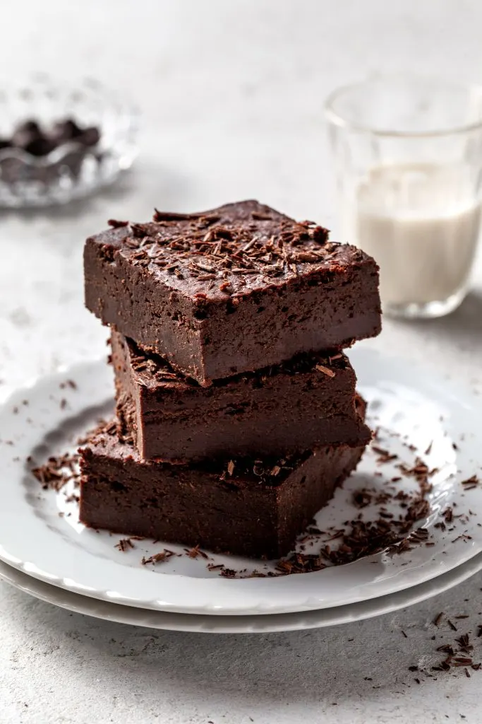 A stack of three sweet potato brownies on a white plate, sprinkled with chocolate shavings. 