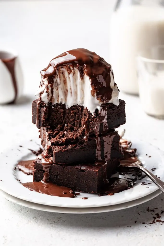 A plate of brownies topped with vanilla ice ream and chocolate sauce, with a forkful missing. 