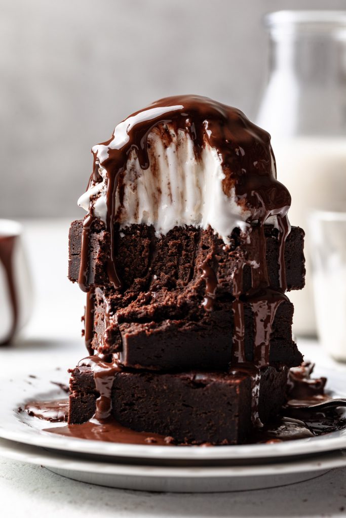 A close up of brownies topped with vanilla ice ream and chocolate sauce with a forkful missing. 